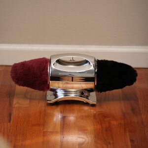 A dual-ended shoe polisher with red and black brushes on a wooden floor.