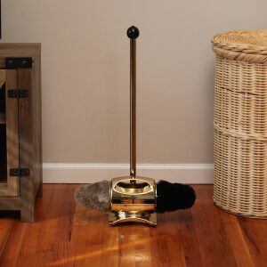 Vintage brass carpet sweeper on wooden floor beside wicker basket.