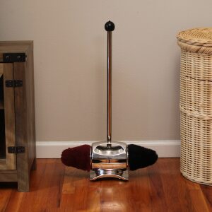 A vintage manual carpet sweeper on a wooden floor beside furniture.